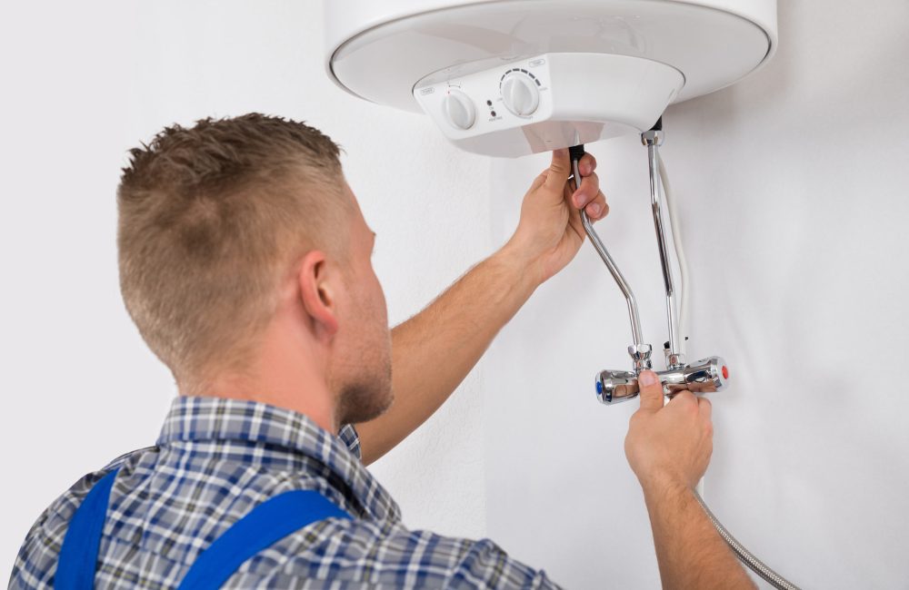 Technician servicing compact electric water heater in Calgary bathroom – Shift Heating and Cooling Services