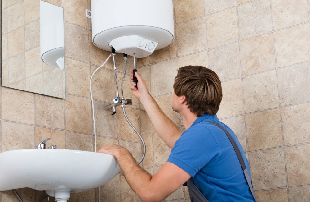 Technician repairing small electric water heater mounted in Calgary bathroom – Shift Heating and Cooling Services