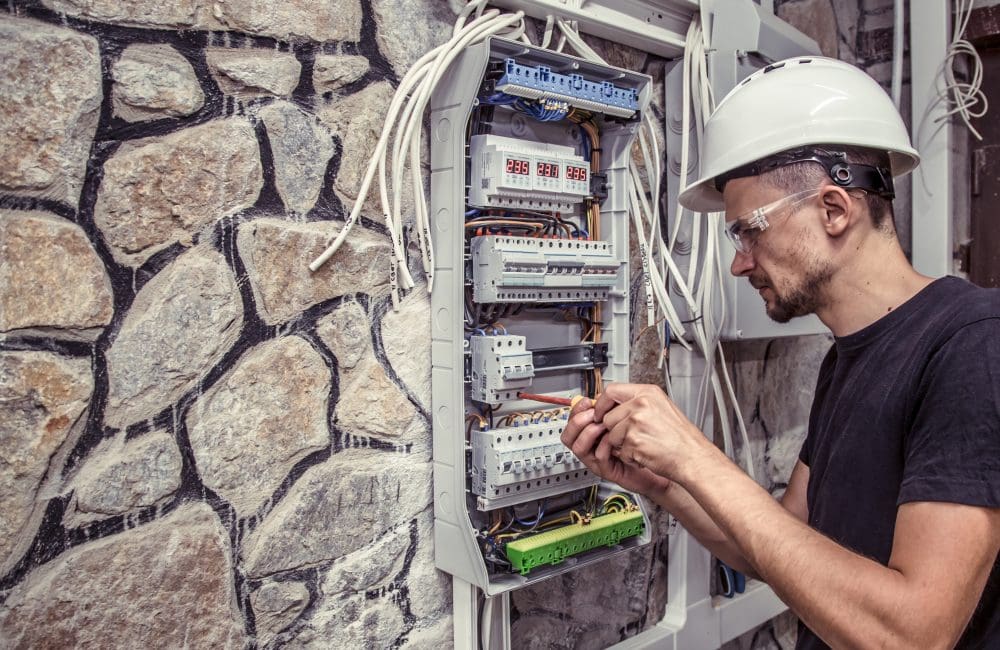 male electrician works in a switchboard with an electrical connecting cab a male electrician works in a switchboard with an electrical connecting cable, connects the equipment with tools, the concept of complex work, space for text